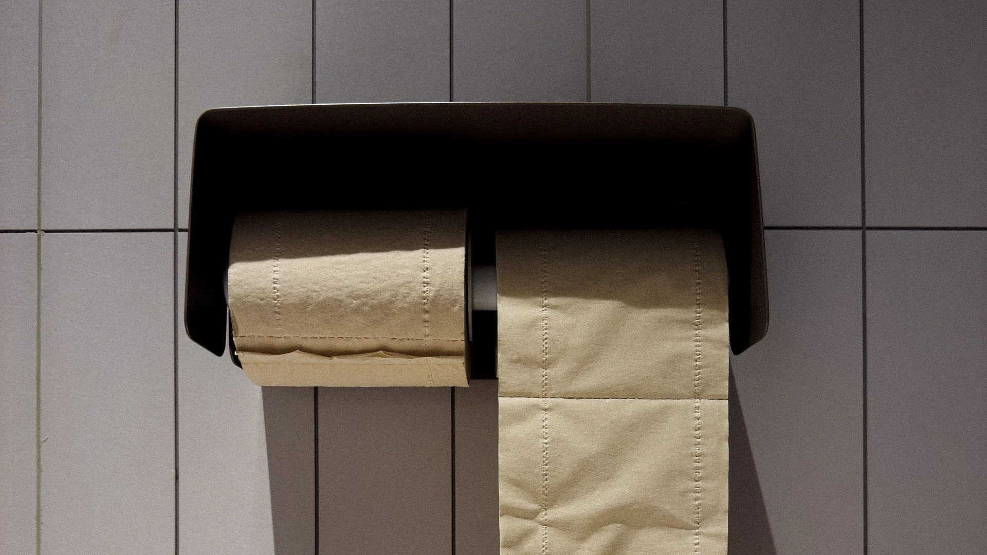 Clean café restroom with a toilet paper dispenser, visible backup toilet paper stock in an open cabinet, and a tidy high-volume restroom setup