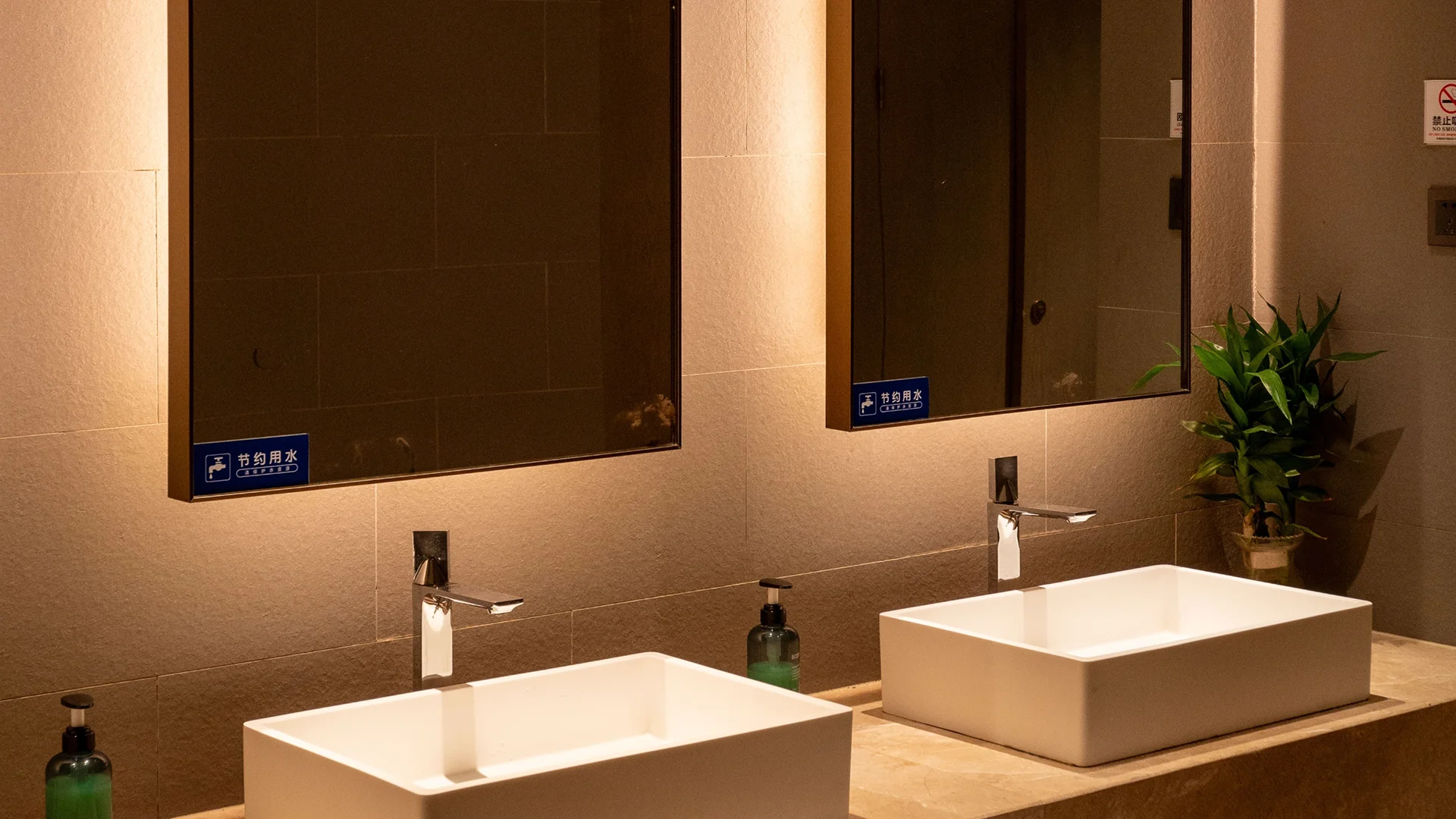 Clean café restroom sink area with two basins, a large mirror, soap dispenser, paper towel dispenser, and tidy countertop