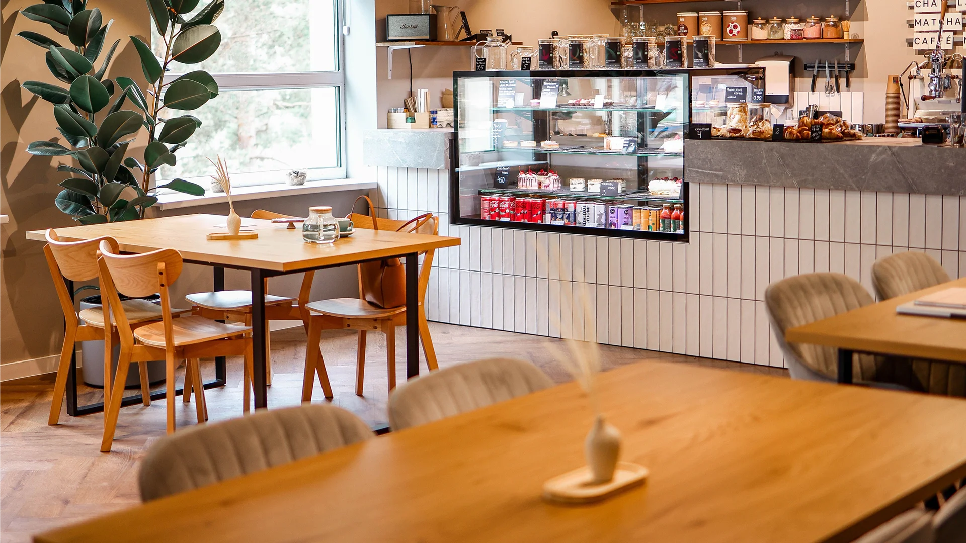 Visitors walking through a modern takeout café, which features a clearly visible refrigerated display case at the entrance and an unobstructed path leading to the order counter