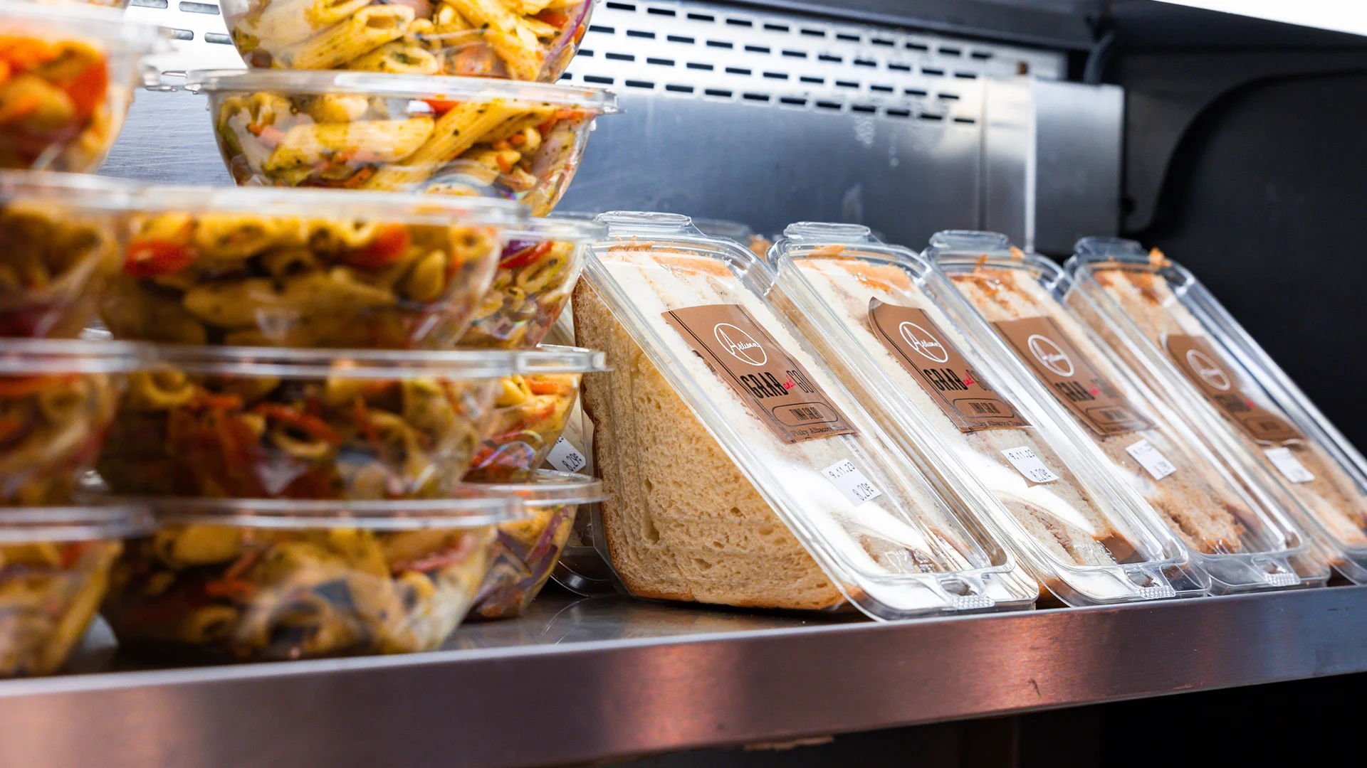 Customer viewing neatly grouped grab-and-go meals, drinks, desserts, and snacks inside a refrigerated café display case
