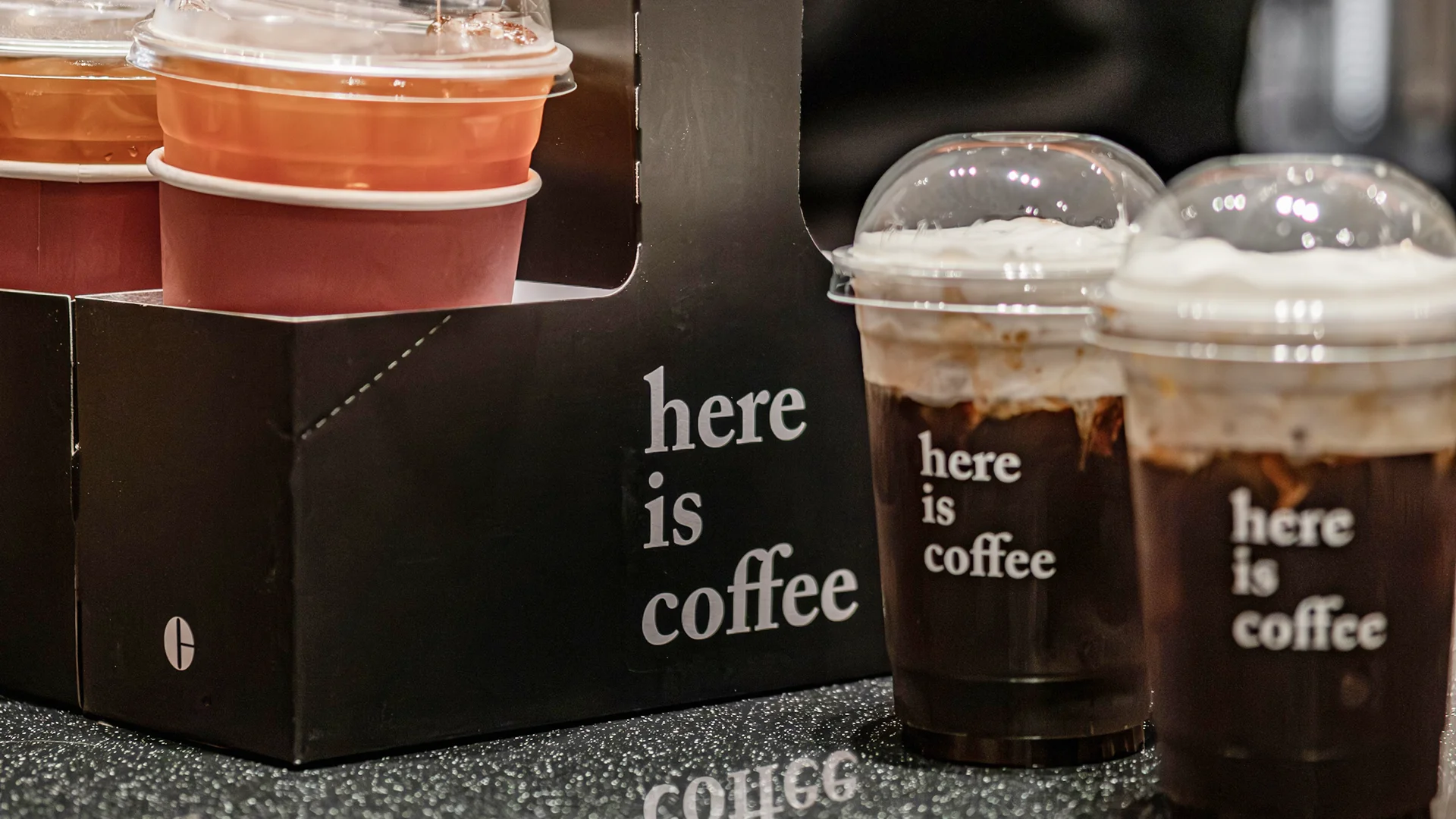 Barista reaching for takeaway lids in a café prep area with cups, bags, napkins, straws, and drink carriers stored close to the espresso station