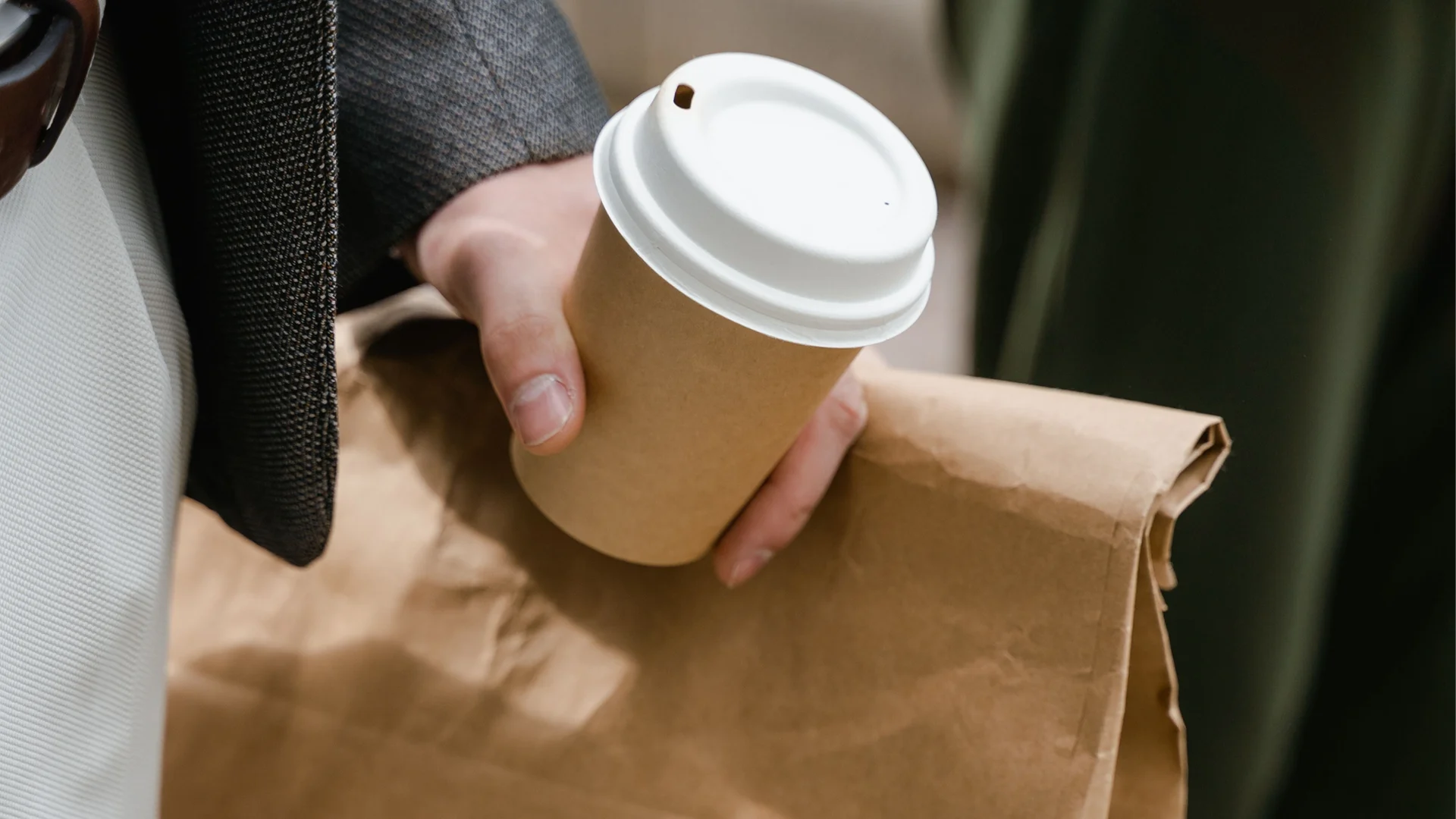 Barista handing two takeaway coffees in a drink carrier to a customer, with a paper bag and napkins on the café counter